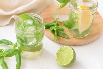 Glass of lemonade with basil on light background