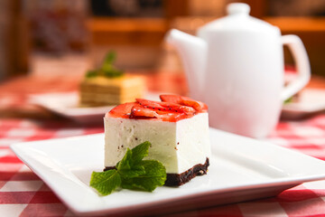 Strawberry cheesecake and fresh strawberries on top served on white plate on a rustic wooden table
