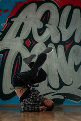 Trendy young man dancer dancing in front of graffiti.