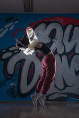 Silhouette of young woman hiphop dancer (breakdancer)dancing on graffiti studio background. Contrast colors.