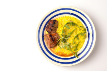 Risotto with meat steak and sauce served in a white plate over white backround.