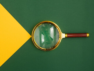 Magnifying glass over green background with yellow paper beam as symbol of insight, discovery and...