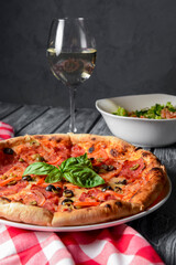 Fresh italian pizza with salami and black olives served with a glass of white wine.