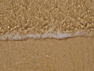 Fototapeta na wymiar Klares Meerwasser wird an einem Strand sanft über den Sand gespült mit copy space
