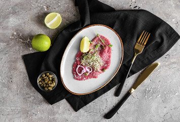 Plate with tasty veal carpaccio, lime and capers on grunge background