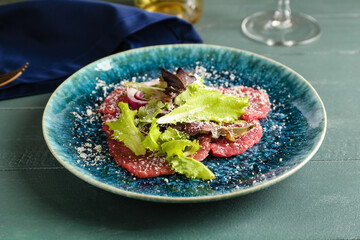 Plate with tasty veal carpaccio on color wooden background