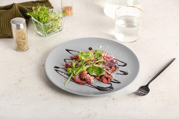 Plate with tasty veal carpaccio, glass of water and fresh sprouts on light background
