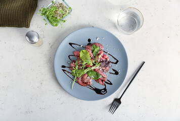 Plate with tasty veal carpaccio, glass of water and fresh sprouts on light background