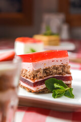 A delicious looking dessert cake served on a white plate. Layered sponge cake with jello layers and mint leaf on top.