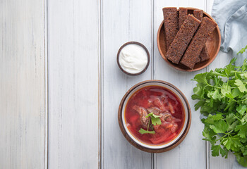 Traditional Ukrainian Russian borsch (beetroot soup) with meat in a black bowl on a  wooden background with slices of fried bread, sour cream and fresh herbs.  copy space