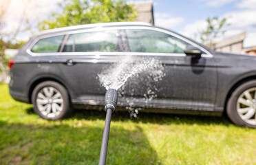 Washing a gray modern car with a manual pressure washer in a summer cottage. Car shampoo for...