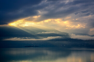 Fototapeta premium Storm Clouds with Sunlight over Brissago Islands on Alpine Lake Maggiore with Mountain in Ticino, Switzerland.