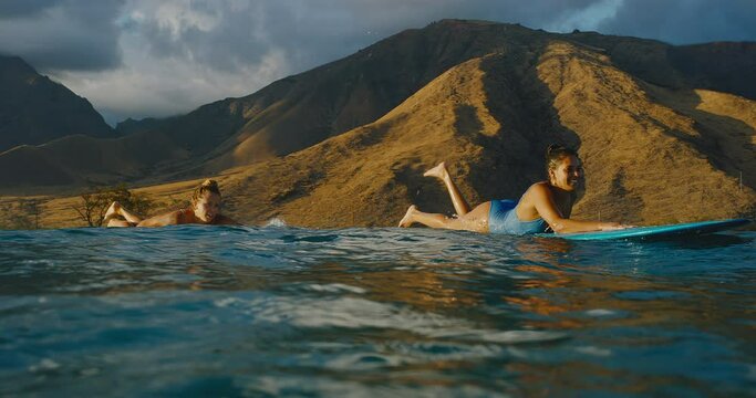 Hawaiian surfer girls paddling out on surfboards at sunset, best friends going surfing, slow motion, lifestyle adventure outdoors