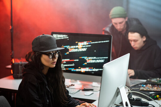 Young Asian woman in hacker attire and two guys decoding information