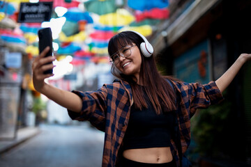 Young smiling woman taking selfie photo outdoors. Beautiful woman listening to music while walking through the city.