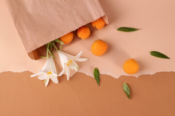 Ripe scattered apricots and lily flowers in a kraft paper bag on a beige background. Zero waste...