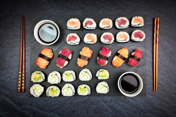 Top view of fish sushi and vegetable sushi with chopsticks and soy sauce on a blackboard. Japanese culture