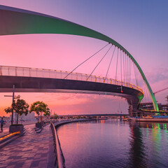 Fototapeta na wymiar Tolerance bridge and promenade embankment along Dubai Creek Canal during majestic colorful sunset light