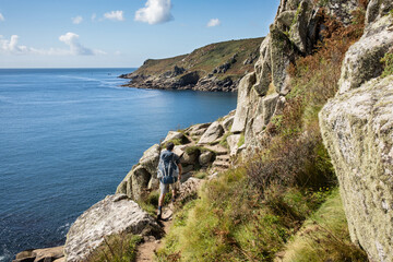 Fototapeta na wymiar Hiker tackles some big stone steps on south west coast path near Lamorna Cove beach, Penzer point in Cornwall