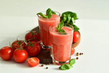 Two glasses of fresh organic tomato juice decorated with raw tomatoes and green leaves of basil on light background.Healthy diet nutrition concept.