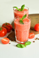 Two glasses of fresh organic tomato juice decorated with raw tomatoes and green leaves of basil on light background.Healthy diet nutrition concept.