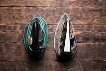 Old fashioned retro electric irons on the brown wooden board flat lay background.