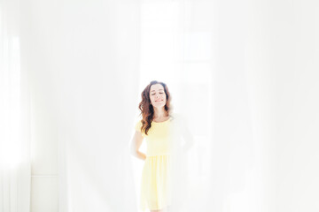 portrait of a beautiful brunette woman in a yellow summer dress by the window