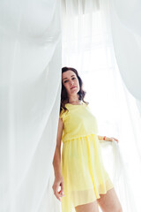 portrait of a beautiful brunette woman in a yellow summer dress by the window