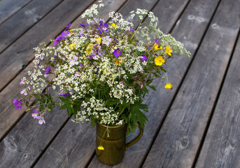 A bouquet of wild summer flowers in a vase on wooden, weathered table.