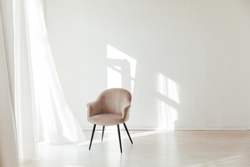 one beige chair in the interior of an empty white room with a window