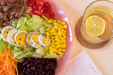 Top view salad plate with different Fresh Vegetables and eggs, glass of water with lemon, and notebook on the table. Healthy lifestyle concept. Detox, diet. Healthy concept lifestyle