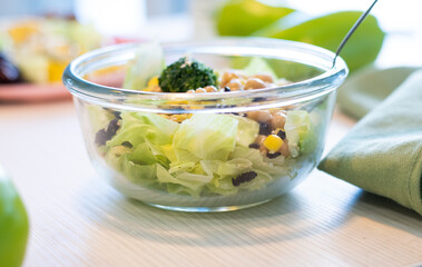 Healthy salad in a glass bowl. Close-up of Chickpea salad, boiled corn, broccoli, lettuce, sesame. Healthy eating planner and peppers on the table. Healthy foods in the background