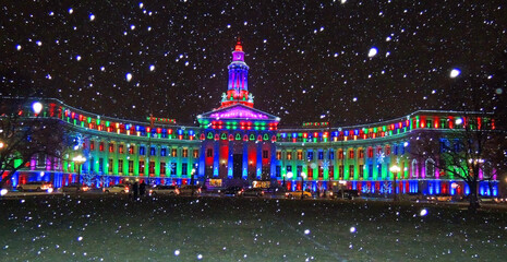  the very colorfully-illuminated   denver city and county building during a snowstorm on christmas...