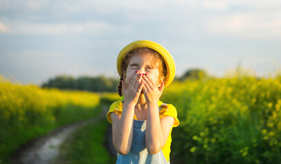 Girl in yellow blooming field covered her nose and face with hands and wrinkled up - an unpleasant...