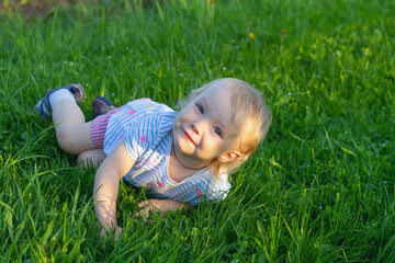 Beautiful baby girl 2 years old lies on the grass in the summer and smiles