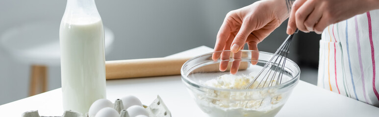 cropped view of woman mixing dough in bowl near milk and chicken eggs, banner.