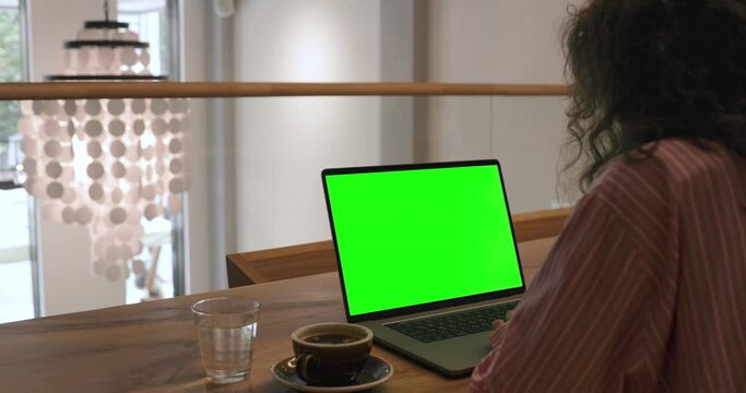 The Female Specialist Works on a Laptop Computer with Mock-up Green Screen. In the Background Evening in the Stylish Caffee Shop. Digital nomad, Freelancer work remoutely.