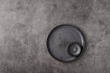 Empty dark plate with saucer set on gray graphite textured background. Top view, copy space