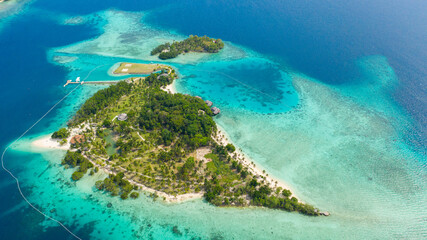 Malipano island with a sandy beach and azure water surrounded by a coral reef and an atoll, aerial view. Philippines, Samal.