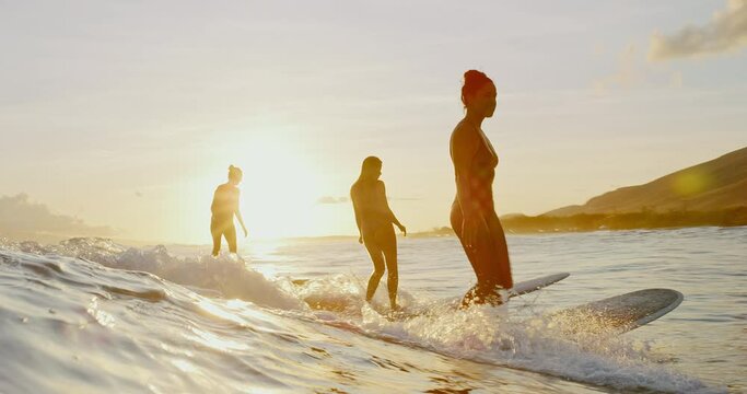 Beautiful girls surfing at sunset, best friends riding wave together, active lifestyle best friends outdoors