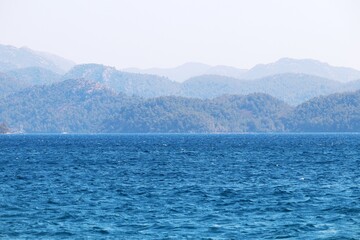 Obraz premium Scenic view to azure sea water and misty mountains covered with forest. Beach vacation, background for summer travel