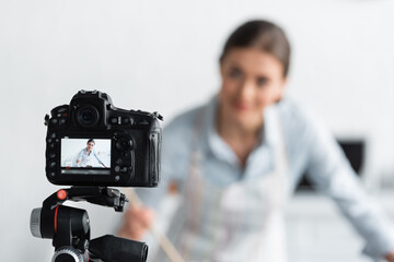 selective focus of digital camera near blurred culinary blogger in kitchen.