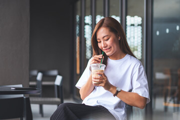 Portrait image of a beautiful young asian woman holding and drinking iced coffee in cafe