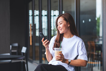 Portrait image of a beautiful young asian woman holding and using mobile phone while drinking coffee in cafe