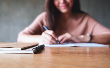 Blurred image of a woman writing on a blank notebook on wooden table