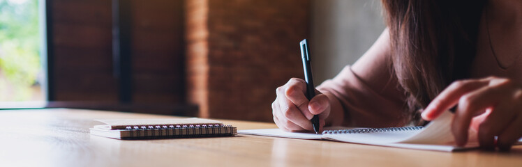 Closeup image of a woman writing on a blank notebook on wooden table