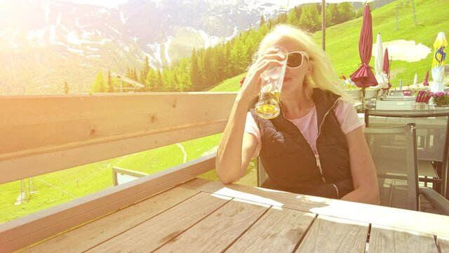 Girl at sunset drinking a draft beer on top Pradaschier park. Station of Churwalden town of Switzerland. Swiss tourist resort for climbing activities and toboggan run in Grisons canton.