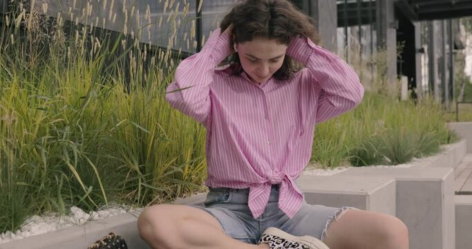 Fashionable white young woman holding mobile phone listening to music by wireless earphones at Asian city urban background. A happy young nonbinary person enjoying music dancing in the street.