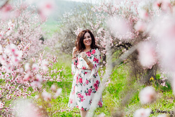 Fototapeta na wymiar Beautiful woman in a dress with flowers walks through the flowering garden in spring