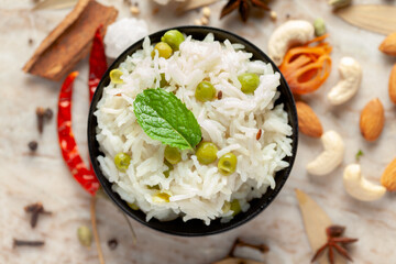 Close-up of Indian Basmati steamed Rice or matar (Pea) pulao or Pulav garnished with fresh green mint leaf in a black bowl.
